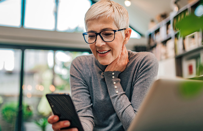 Person using her phone while using a laptop.