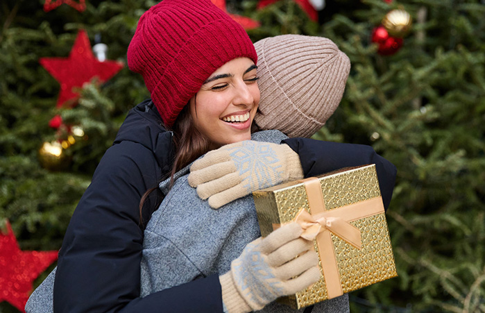 Person holding a Christmas present hugging a friend.